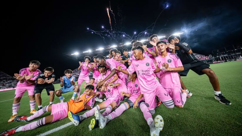 Soccer players in pink uniforms celebrating together on the field after a match.